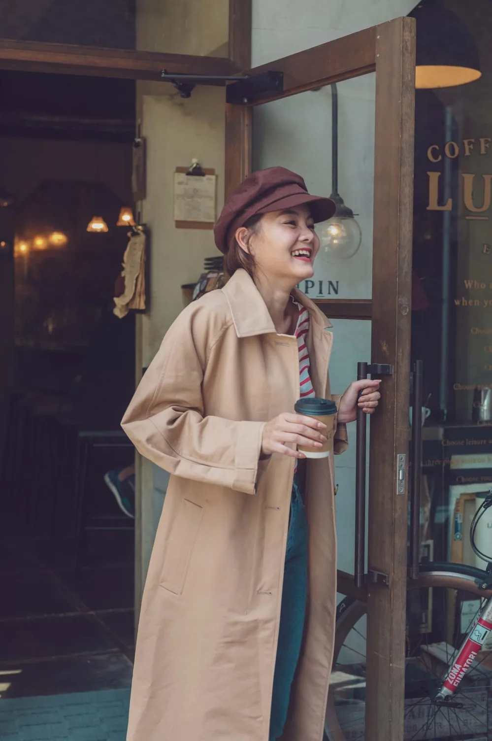 A woman steps out of a coffee shop, coffee in hand